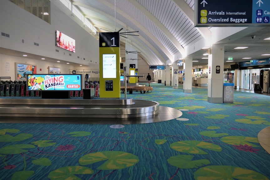 Baggage carousels, digital ads, screens, and large fans in an airport terminal building.