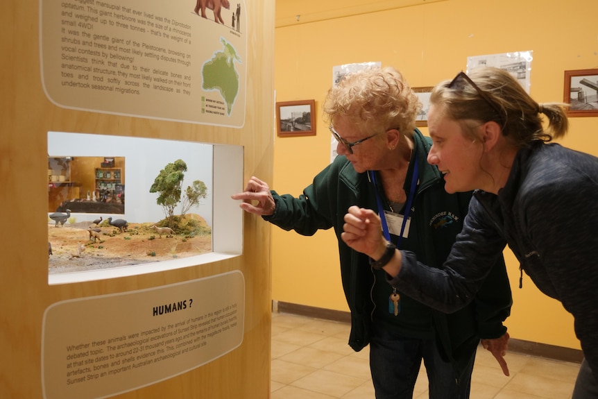 two women pointing at a window in the Megafauna display