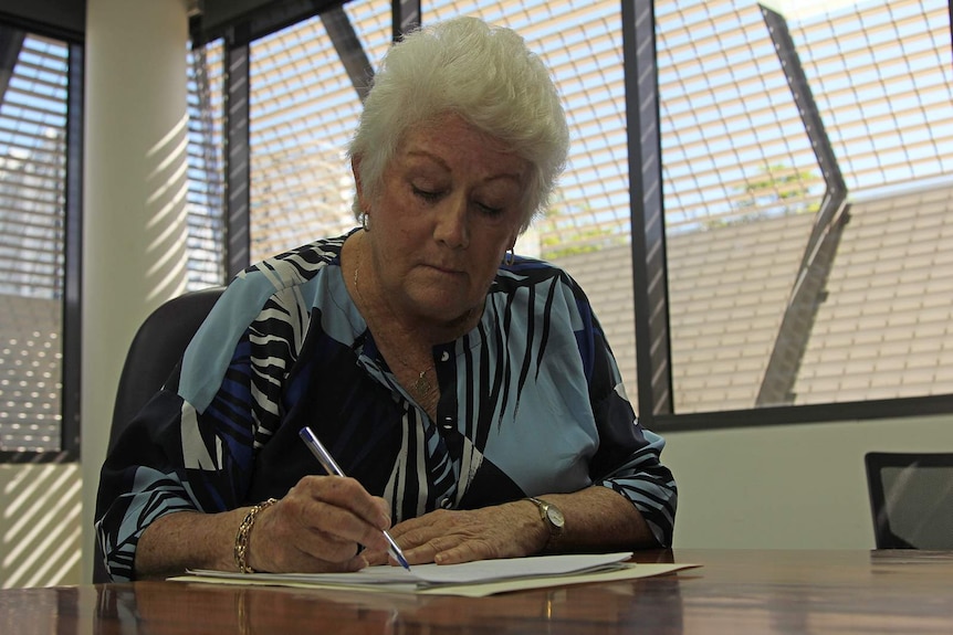 COTA NT CEO, Sue Shearer, sits at a table writing on some paper.