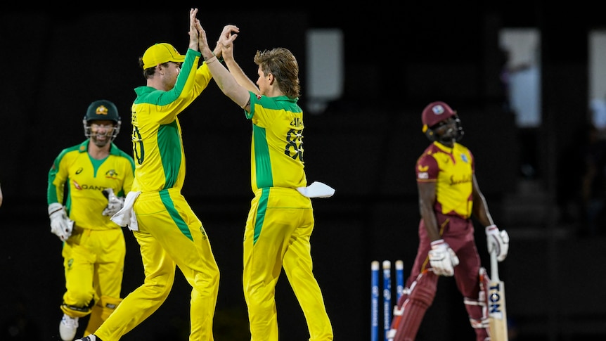 Two Australians do a double high-five to celebrate a West Indies wicket as the batsman trudges off in a T20I.