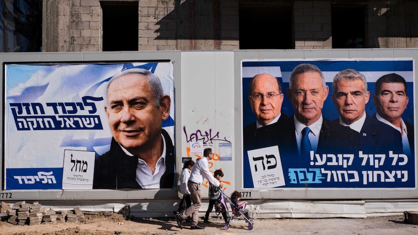 From the other side of the street, you see a man pushing a stroller walking past 2019 Israeli election politicians' posters