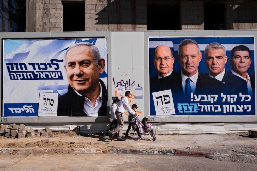 From the other side of the street, you see a man pushing a stroller walking past 2019 Israeli election politicians' posters