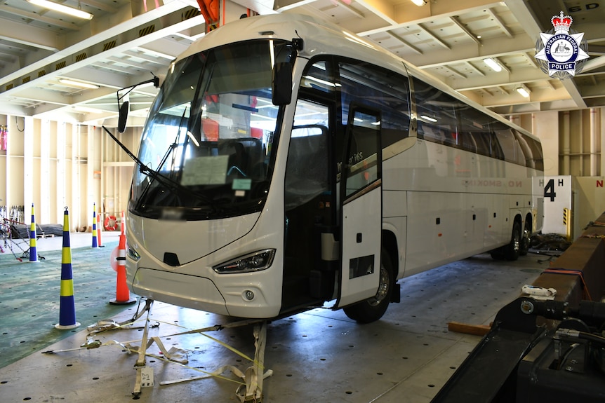 A luxury bus parked inside a warehouse next to a tarp and witcher's cones