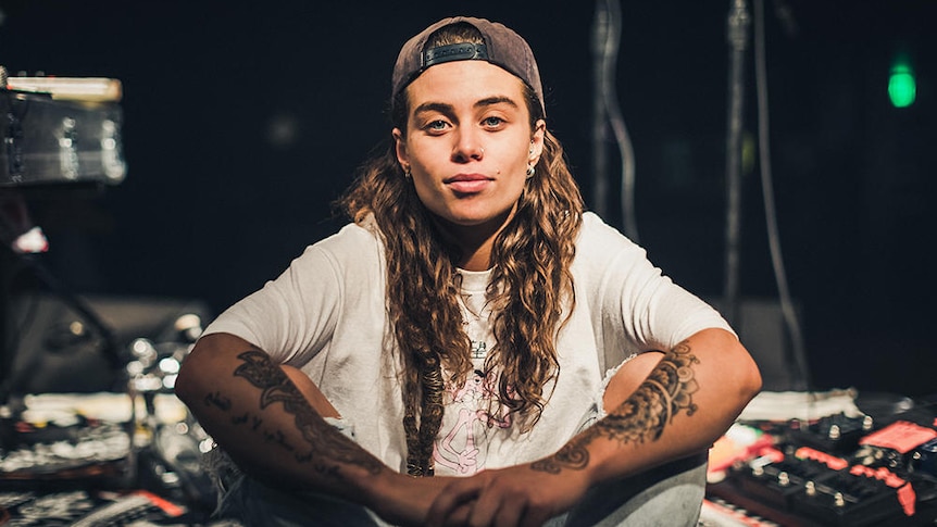 Image of Tash Sultana seated on floor surrouned by musical gear