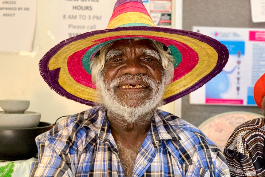 An Indigenous man smiles wide while trying on a colour sombrero