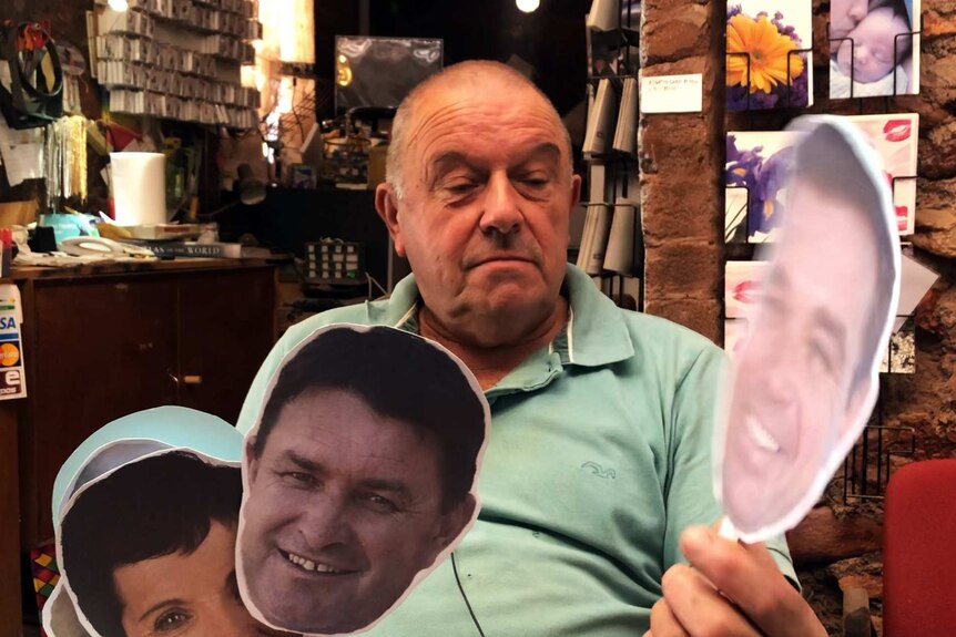 A middle-aged man holds a hand full of cut outs of people's faces.