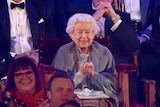 The Queen sits in the stands watching the Jubilee finale smiling with hands clasped. 