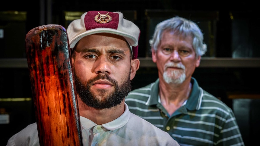 Two aboriginal men looking at the camera, one with a cricket bat