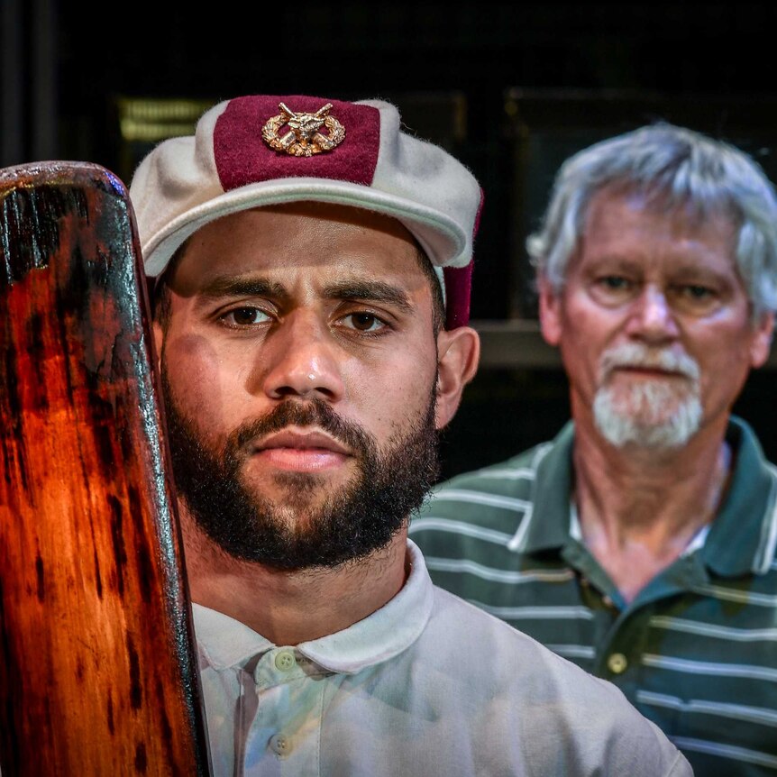 Two aboriginal men looking at the camera, one with a cricket bat