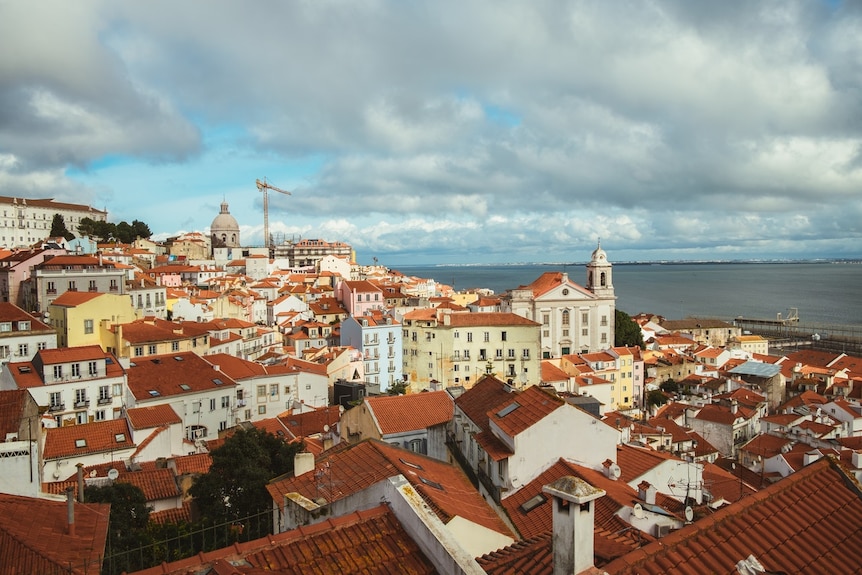 A wide shot of Lisbon, with many houses with red roofs looking out to sea