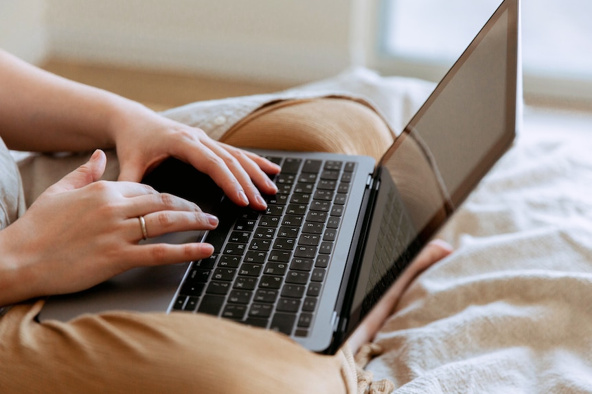 Close up of a woman's hands who is typing on a laptop in bed, working after hours.