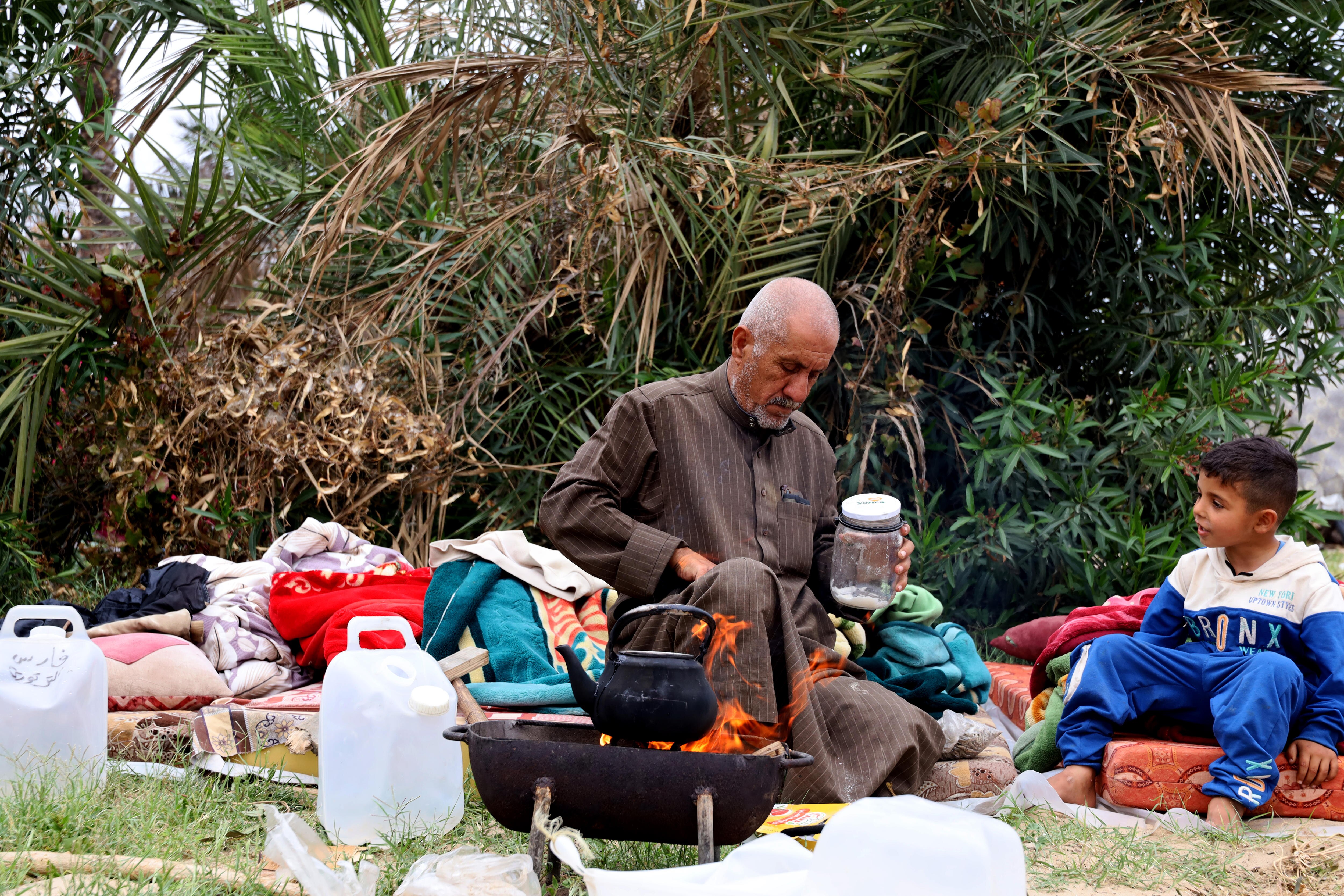 A man sits in front of a campfire as a young boy sits next to him.