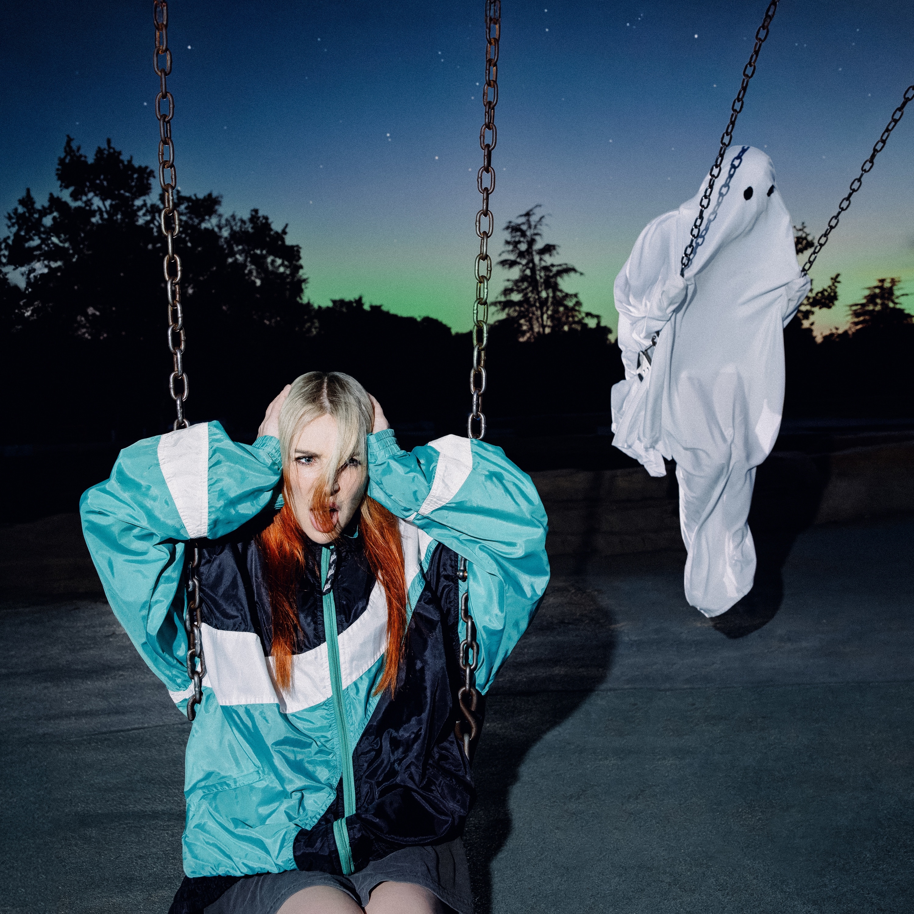 Girl holding ears on swing. Person in a sheet looking like a ghost mid-air on adjacent swing