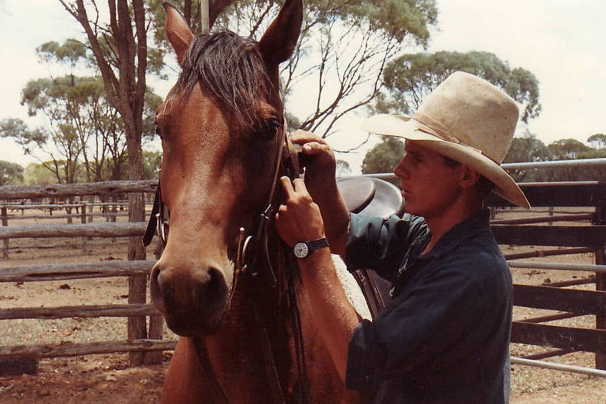 A man in a cowboy hat saddles a horse