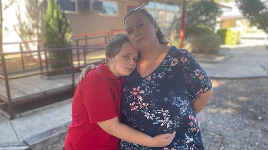 little girl in red school uniform hugs lady in blue top 