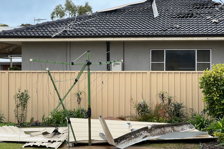 A badly damaged Hills hoist stands amongst sheets of metal in a backyard