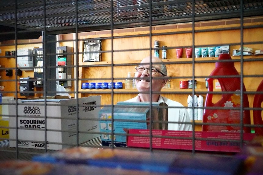 A man smiles as he looks at product on a supermarket shelf.