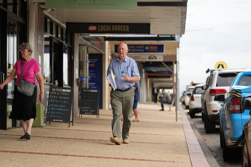 An older bald white man walking on a footpath in a regional town