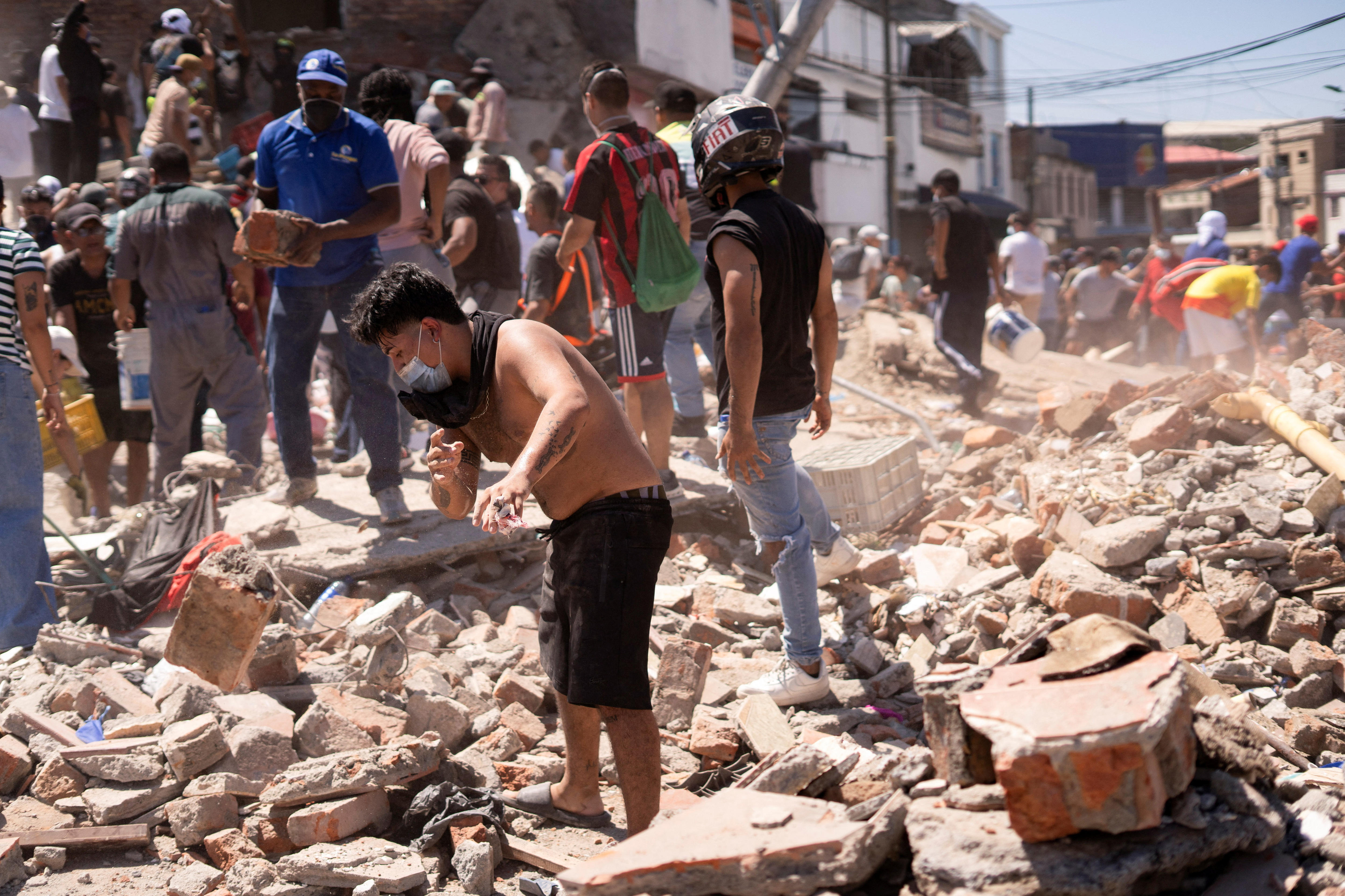 A young man picking through debris strewn on the ground of a city street.