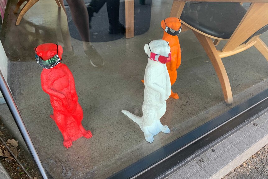 Meerkat statues wearing masks in a shop window.