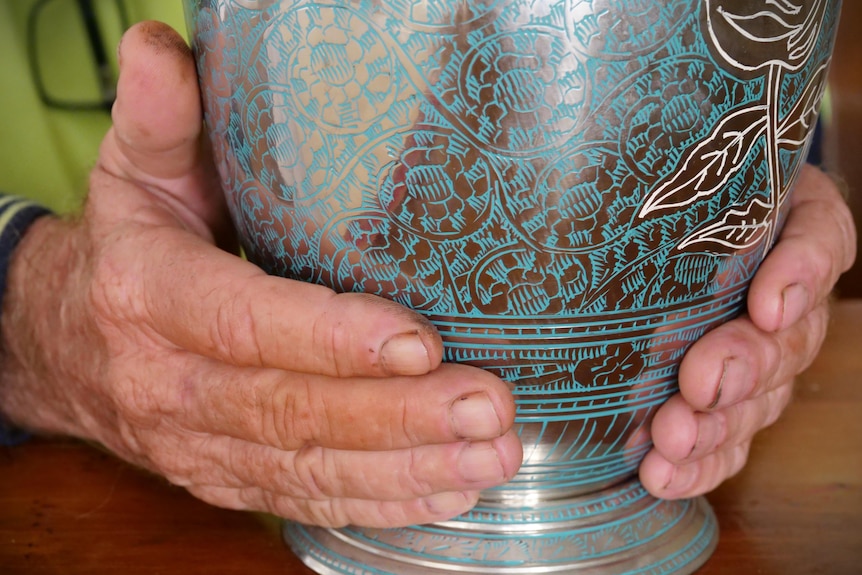 A man's hands holding a silver and blue urn