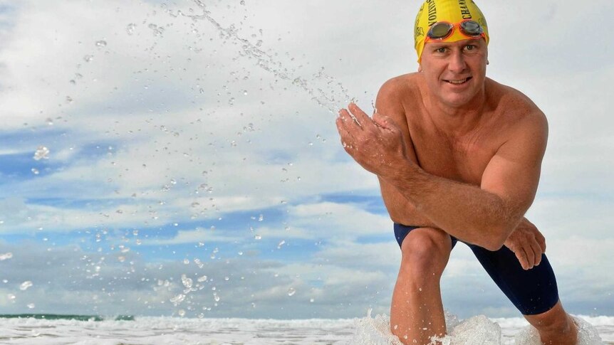 Man in swim cap stands in ocean flicking water in the air