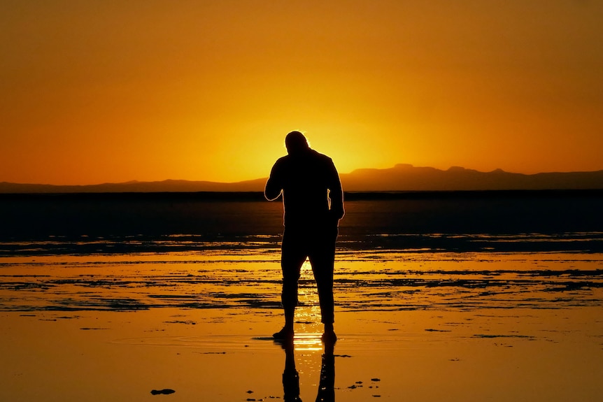 A silhouette of a man on water with a sunset in the background