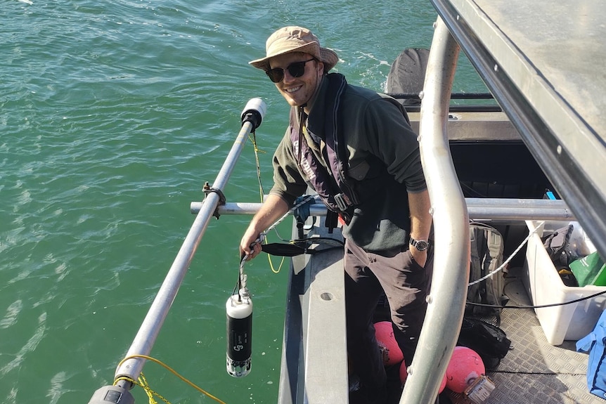 A researcher on a boat on a river, holding a piece of equipment.