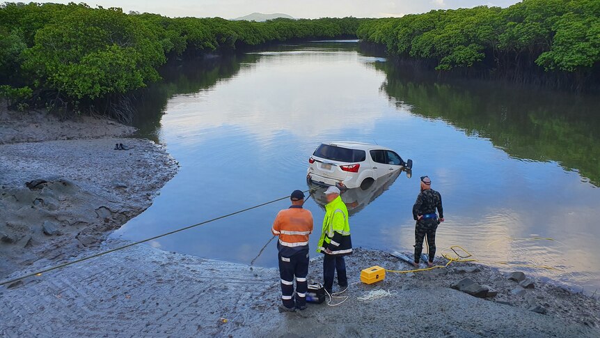 A car gets pulled out of a creek as three people watch on.