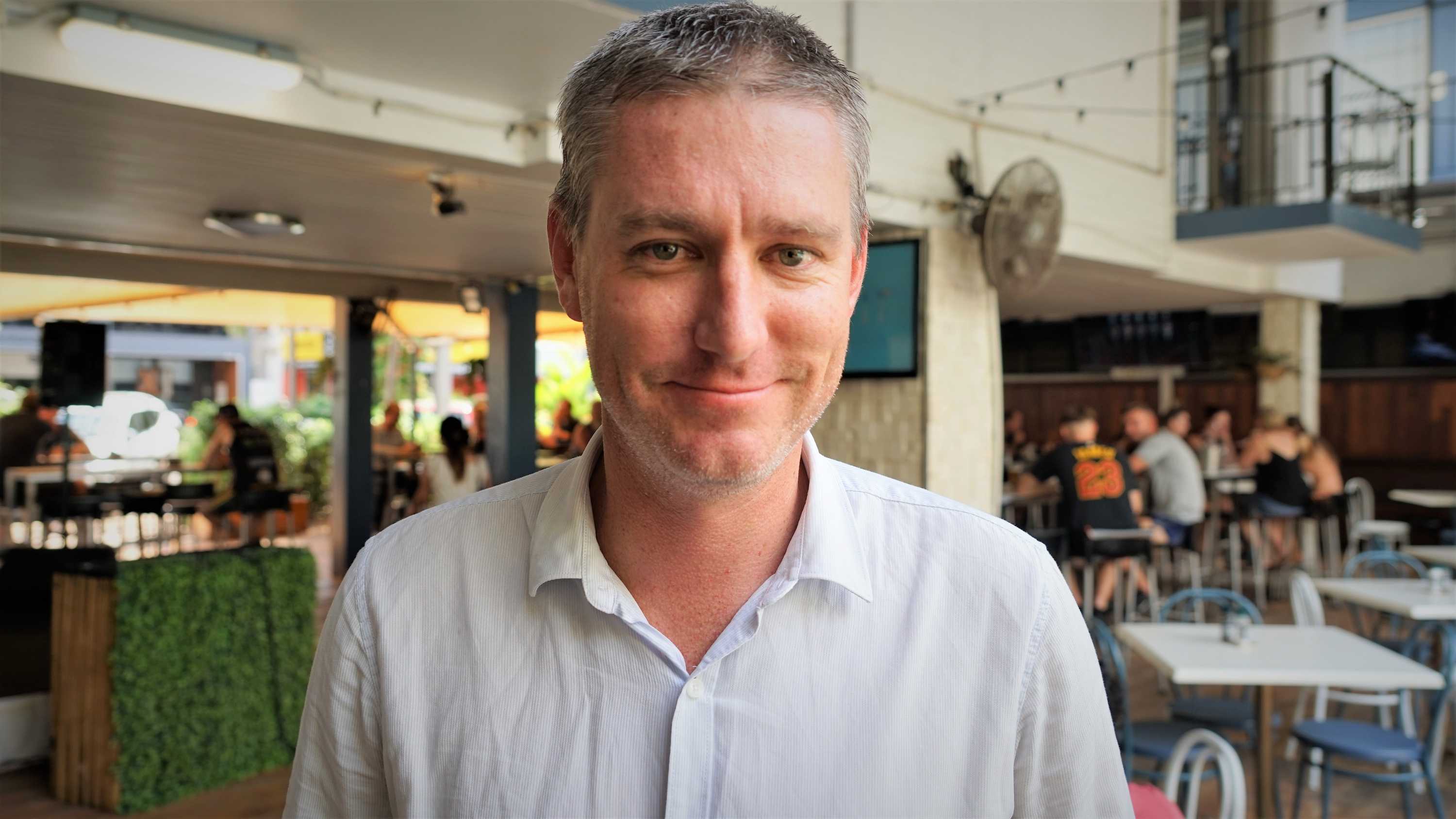 posed headshot of man standing on a pub veranda smiling.  Top button open