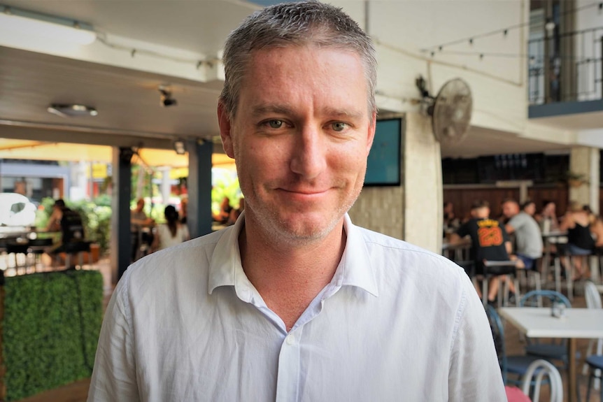 A man standing on a pub veranda smiling. Top button open