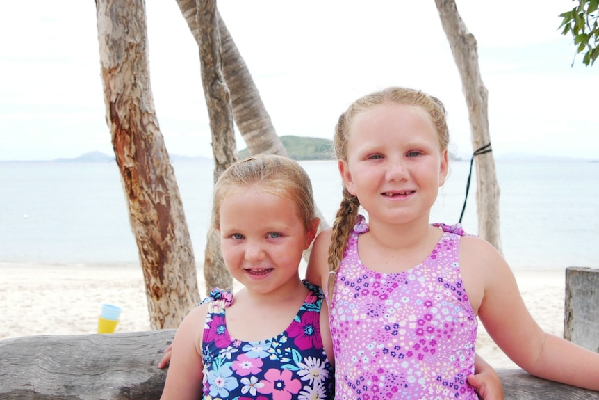 Two young girls stand together on the beach