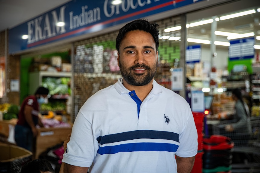 A man with a beard wearing a white polo shirt in a supermarket