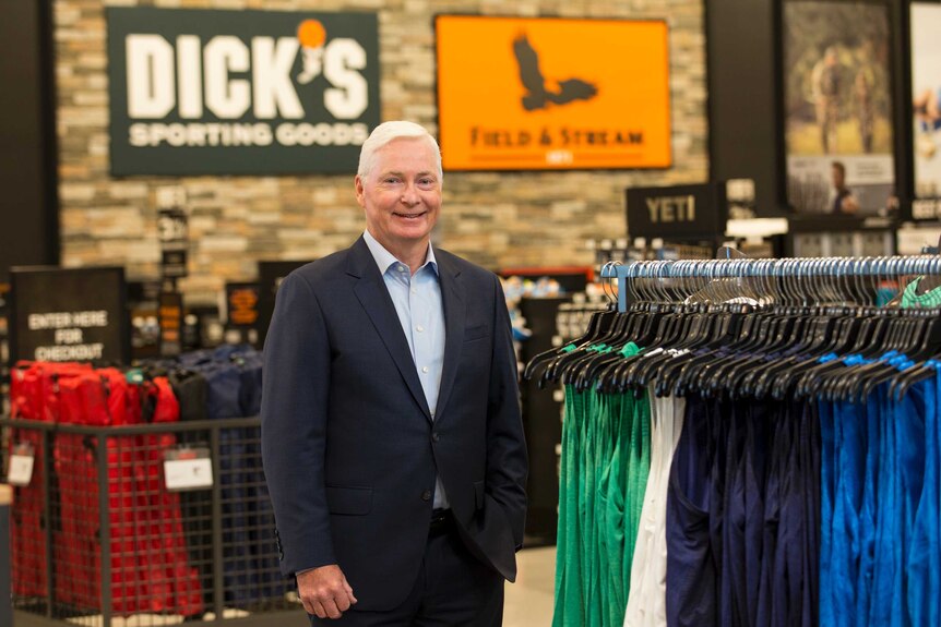 Edward Stack poses for a photo inside a store with clothes on racks next to him.