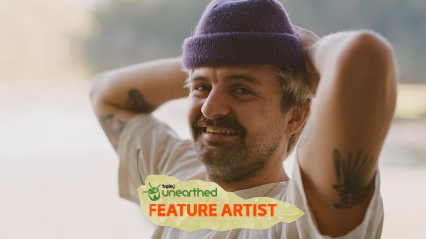 Adam Newling, a young man wearing a purple beanie, smiles at the camera with his hands behind his head.