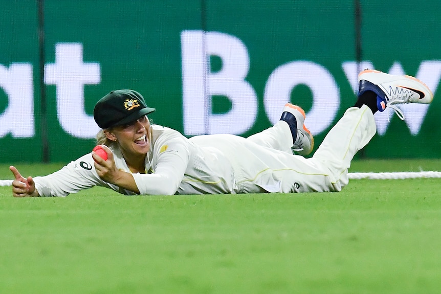 Ash Gardner smiles while lying on her stomach and holding the ball in her left hand