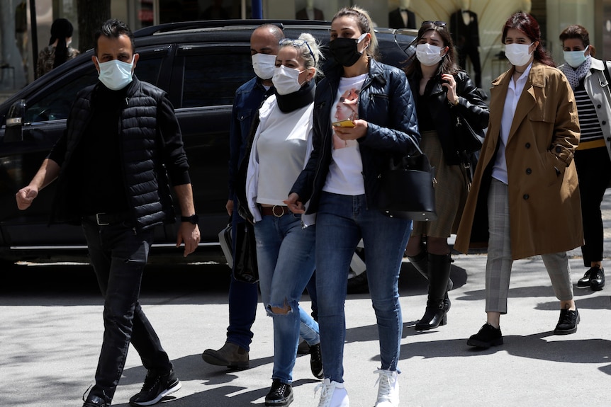 Eine Gruppe von Menschen mit Masken geht die Straße entlang.