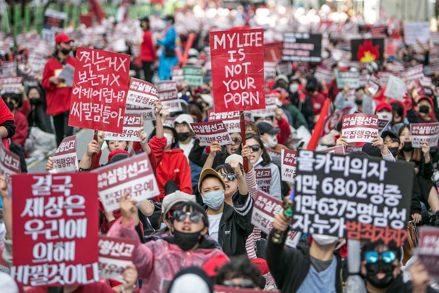 South Korean people protesting in the street; one holds a sign in English saying 'my life is not your porn'.