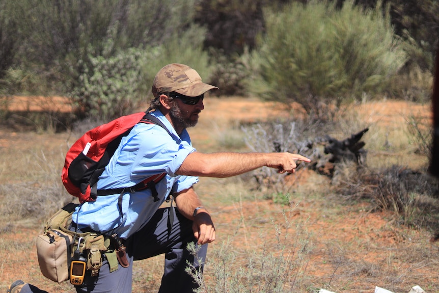 A man in a blue shirt and army camo cap bends down on one knee at points