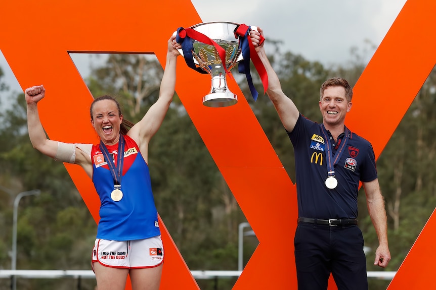 Daisy Pearce dan Mark Stinear tersenyum saat mengangkat piala premiership