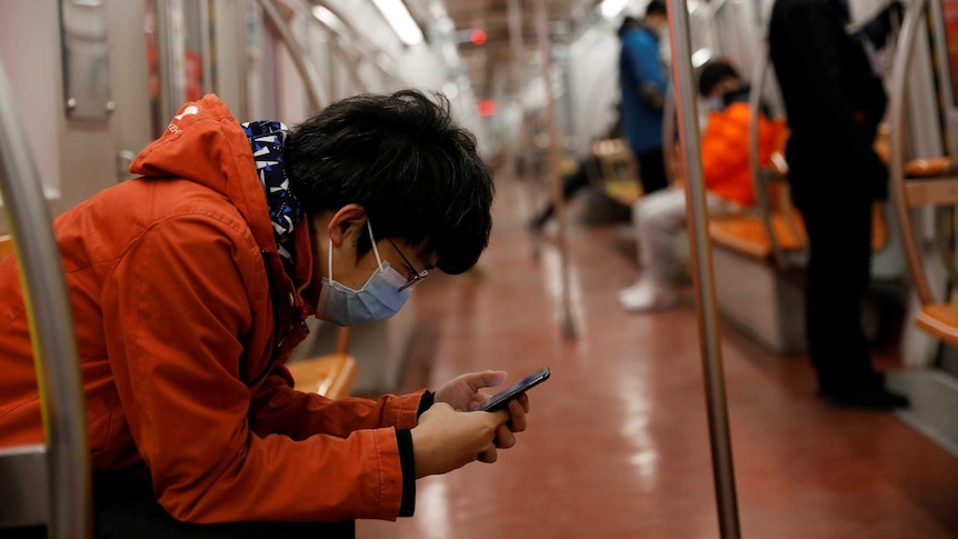 A man wearing a face mask checks his mobile phone while riding a subway in the morning after the extended Lunar New Year holiday