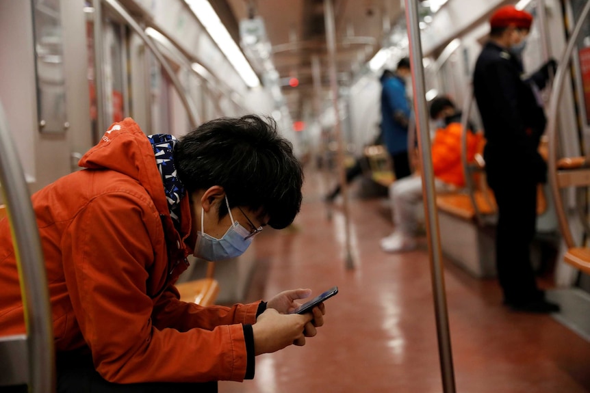 A man wearing a face mask checks his mobile phone while riding a subway in the morning after the extended Lunar New Year holiday