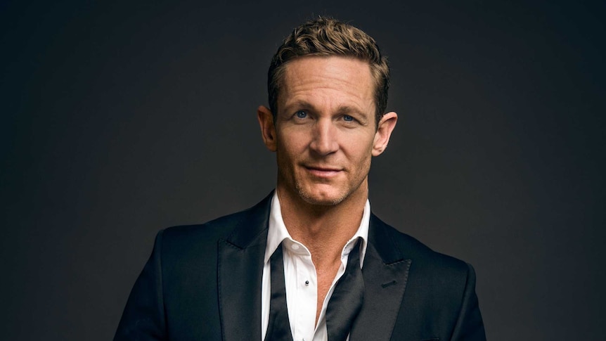 Actor and singer David Harris wearing a tuxedo and standing in front of a grey backdrop.