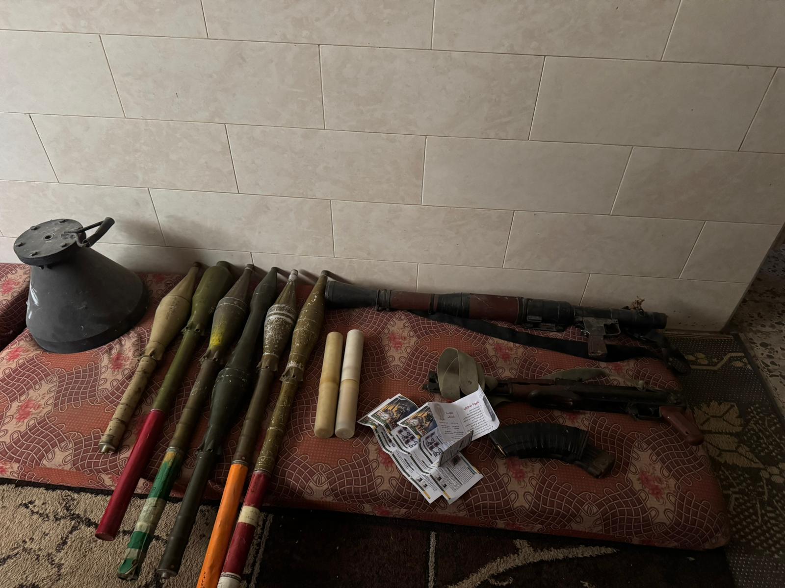A cache of rockets, rocket launchers and weapons laid out on a cushion on the ground.