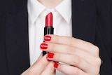 A woman's hands wearing red nail polish winds up a red lipstick