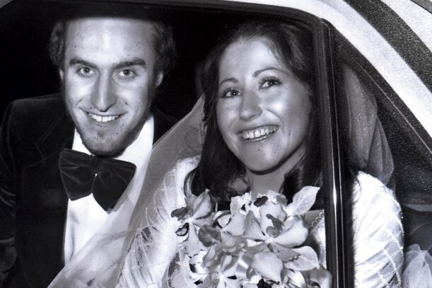 Black and white photo of bride and groom beaming from the backseat of their wedding car