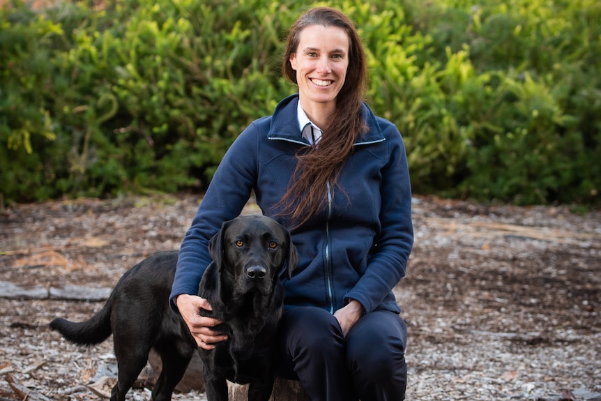 Dr Anne-Lise Chaber knelling next to a black dog