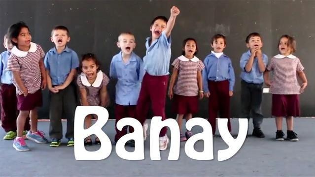 Small children stand in line shouting, superimposed word "Banay"