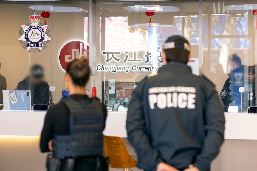 Two federal police officers are shown from behind at a Changjiang Currency Exchange outlet.