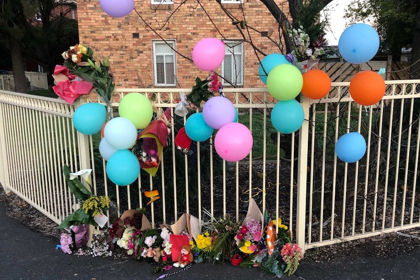 colourful balloons and flowers tied to a fence outside commission flats